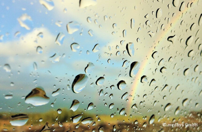 wechselhaftes Wetter Glasscheibe mit Regentropfen und Regenbogen