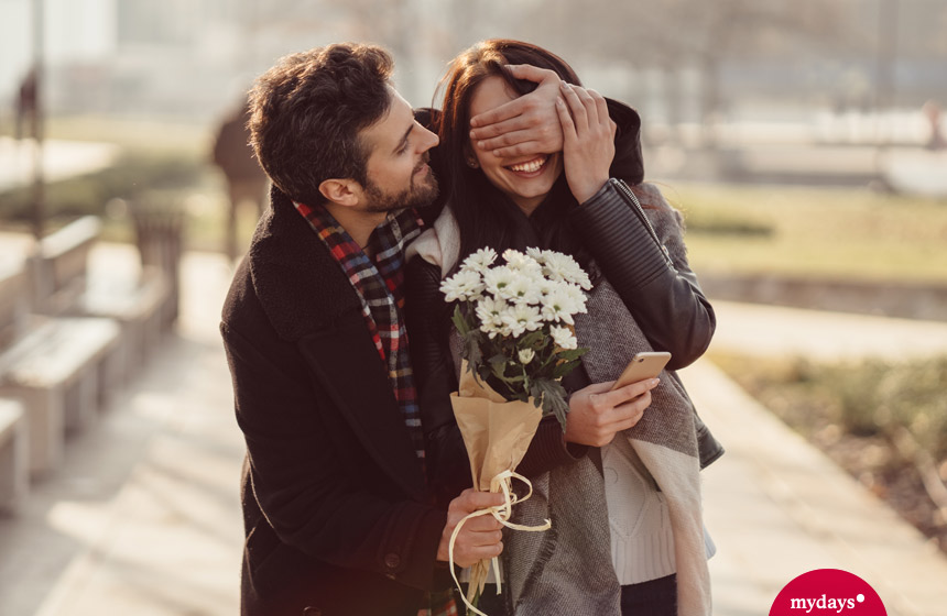 Mann überrascht Frau mit Blumenstrauß.