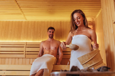 Frau macht Saunaaufguss mit Mann im Hintergrund