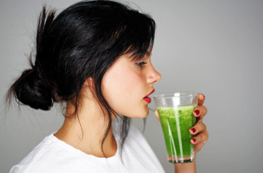 Frau mit schwarzen Haaren trinkt grünen Smoothie