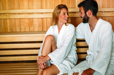 Mann und Frau im Bademantel lächeln sich in der Sauna an
